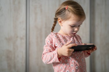 Bir beyaz çocuk cep telefonunu evde tutuyor video oyunları oynuyor ve büyüyen teknoloji bağımlılığı kavramı online tarama veya video izlemek için uygulama kullanıyor