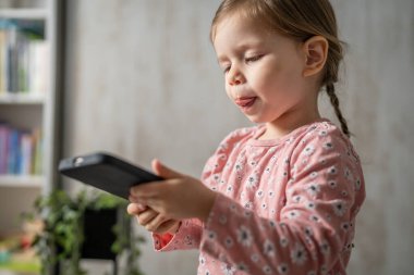 Bir beyaz çocuk cep telefonunu evde tutuyor video oyunları oynuyor ve büyüyen teknoloji bağımlılığı kavramı online tarama veya video izlemek için uygulama kullanıyor