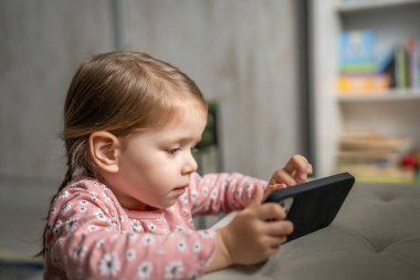 Bir beyaz çocuk cep telefonunu evde tutuyor video oyunları oynuyor ve büyüyen teknoloji bağımlılığı kavramı online tarama veya video izlemek için uygulama kullanıyor