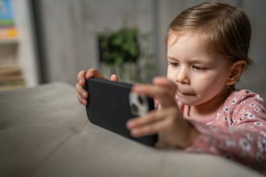 Bir beyaz çocuk cep telefonunu evde tutuyor video oyunları oynuyor ve büyüyen teknoloji bağımlılığı kavramı online tarama veya video izlemek için uygulama kullanıyor