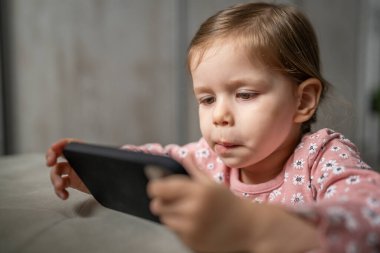 Bir beyaz çocuk cep telefonunu evde tutuyor video oyunları oynuyor ve büyüyen teknoloji bağımlılığı kavramı online tarama veya video izlemek için uygulama kullanıyor