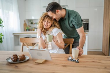 Kafkasyalı mutlu çift, yetişkin erkek ve kadın karı ve koca sabah rutini dijital tablet kullanırken bir fincan kahve ya da çay içiyorlar ve evlerinde sevişiyorlar.