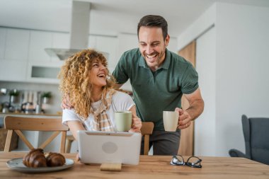 Kafkasyalı mutlu çift, yetişkin erkek ve kadın karı ve koca sabah rutini dijital tablet kullanırken bir fincan kahve ya da çay içiyorlar ve evlerinde sevişiyorlar.