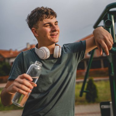 Beyaz tenli bir genç, plastik su şişesini açık tutuyor ve açık havada güneşli su ve sağlıklı yaşam tarzı konsepti fotokopi çekerken içmeye hazırlanıyor.