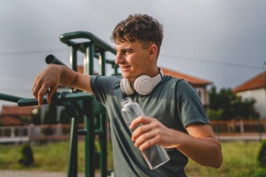 Beyaz tenli bir genç, plastik su şişesini açık tutuyor ve açık havada güneşli su ve sağlıklı yaşam tarzı konsepti fotokopi çekerken içmeye hazırlanıyor.