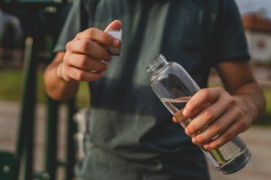 Beyaz tenli bir genç, plastik su şişesini açık tutuyor ve açık havada güneşli su ve sağlıklı yaşam tarzı konsepti fotokopi çekerken içmeye hazırlanıyor.