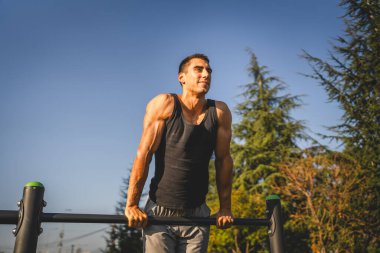 Açık spor salonunda antrenman yapan genç bir beyaz erkek sporcu şehirde yaz günü sağlıklı yaşam tarzı ve dinlenme eğitimi alıyor.