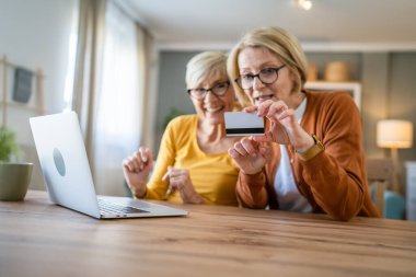 İki olgun yaşlı kadın büyükanne kadın evde oturup online alışveriş siteleri için kredi kartı ya da banka kartı kullanıyor. Bir şeyler satın alıyorlar. Dijital tablet kullanıyorlar. Gerçek insanlar yer kopyalıyor.