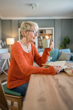 Yetişkin, yaşlı, Kafkasyalı, emekli, kısa saçlı, kitap okuyan bir kadın gözlük takıyor.