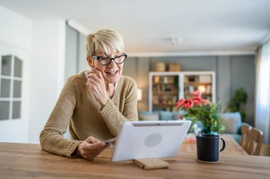 Yetişkin bir yaşlı kadın büyükanne evde oturup online alışveriş siteleri için kredi kartı ya da banka kartı kullanıyor. Bir şeyler satın alıyor. Dijital tablet kullanıyor. Gerçek insanlar yer kopyalıyor.