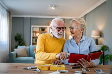 Senior couple man and woman husband wife looking family photos album caucasian old male and female grandfather and grandmother happy smile at home with old pictures real people copy space clipart