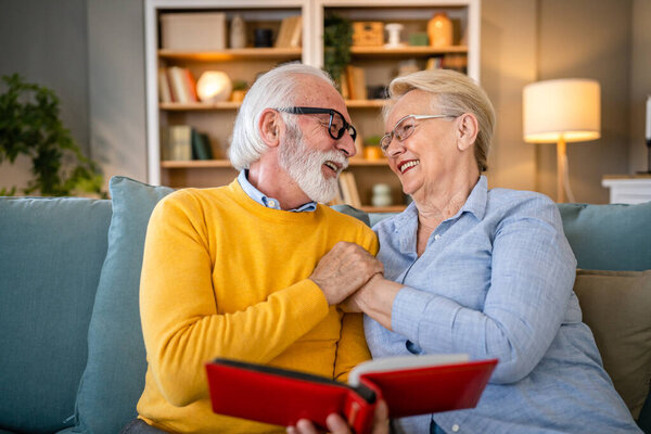 Senior couple man and woman husband wife looking family photos album caucasian old male and female grandfather and grandmother happy smile at home with old pictures real people copy space