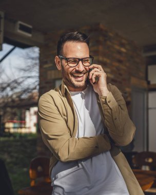 Güneşli bir günde dışarıda sakallı ve gözlüklü yetişkin bir adam mutlu bir gülümseme ile cep telefonunu kullanarak konuşma yeri fotokopisi çeken gerçek insanlar yapıyor.