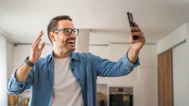 Beyaz erkek mutlu adam görüntülü sohbet görüşmesi yapıyor. Evdeki akıllı cep telefonundan.