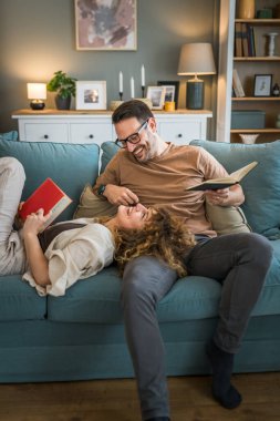Yetişkin çift, beyaz karı koca, ilişki içinde. Gerçek bir kitap. Evdeki kanepede kitap tutuyorlar.