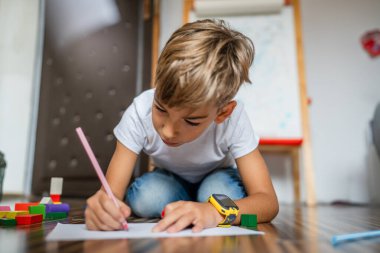 Bir küçük beyaz çocuk evde pastel boyayla resim çiziyor.
