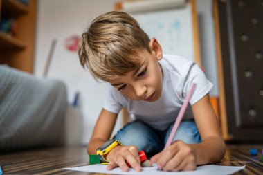 Bir küçük beyaz çocuk evde pastel boyayla resim çiziyor.