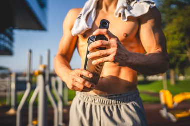 Beyaz tenli genç bir erkek sporcu açık hava spor salonunda çalışırken fren yapıyor. Elinde destek malzemesi tutuyor. Kendine güveni tam, güçlü, güçlü bir kopya alanı var.