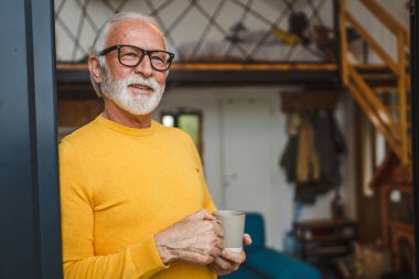Yaşlı, beyaz, sakallı ve gözlüklü bir adam gün içinde balkonda mutlu bir gülümseme içinde kahvenin fotokopi makinesinin günlük konseptini tutuyor.