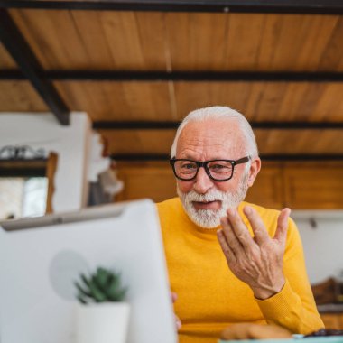 Üst düzey beyaz adam evde video görüşmesi yapmak için dijital tablet kullanıyor.