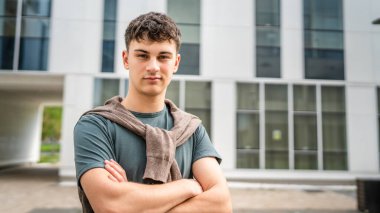 Genç, yetişkin, beyaz bir genç, dışarıda durup fotoğraf çekiyor. Kameraya bakıyor. Kendine güveni tamdır.