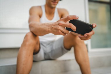 Dışarıdaki genç adamın portresi video oyunları oynamak için kulaklık ve akıllı telefon kullanıyor.