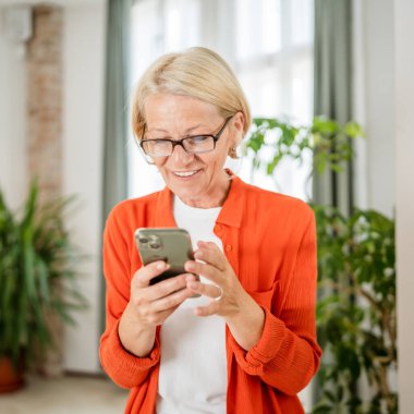 Yetişkin, beyaz, sarışın bir kadın cep telefonu akıllı telefonu kullanarak mesaj atıyor. Mutlu, kendine güvenen, gerçek insanlar uzayı kopyalıyor.