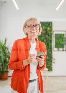 Yetişkin, beyaz, sarışın bir kadın cep telefonu akıllı telefonu kullanarak mesaj atıyor. Mutlu, kendine güvenen, gerçek insanlar uzayı kopyalıyor.