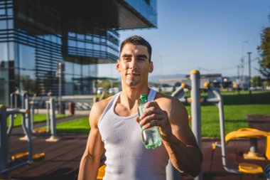 Beyaz tenli bir erkek sporcu plastik su şişesini açık tutuyor ve açık havada güneşli su ve sağlıklı yaşam tarzı konsepti fotokopi çekerken içmeye hazırlanıyor.