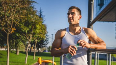 Beyaz tenli bir erkek sporcu plastik su şişesini açık tutuyor ve açık havada güneşli su ve sağlıklı yaşam tarzı konsepti fotokopi çekerken içmeye hazırlanıyor.