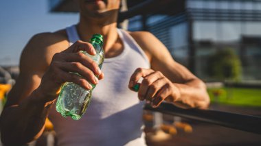 Beyaz tenli bir erkek sporcu plastik su şişesini açık tutuyor ve açık havada güneşli su ve sağlıklı yaşam tarzı konsepti fotokopi çekerken içmeye hazırlanıyor.