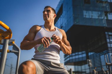 Beyaz tenli bir erkek sporcu plastik su şişesini açık tutuyor ve açık havada güneşli su ve sağlıklı yaşam tarzı konsepti fotokopi çekerken içmeye hazırlanıyor.