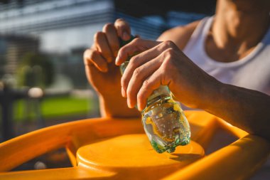 Beyaz tenli bir erkek sporcu plastik su şişesini açık tutuyor ve açık havada güneşli su ve sağlıklı yaşam tarzı konsepti fotokopi çekerken içmeye hazırlanıyor.