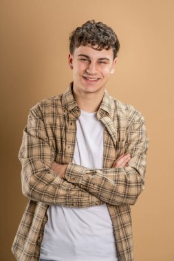 20 yaşında beyaz bir adamın portresi. Badem rengi stüdyo arkaplanının önünde kameraya bakıyor. Gülümsüyor.