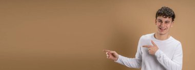 20 yaşında beyaz bir adamın portresi. Almond Renkli Stüdyo Arkaplanı 'nın önünde kameraya bakıyor. Fotokopi uzayında günlük gömlek giyip gülümsüyor.