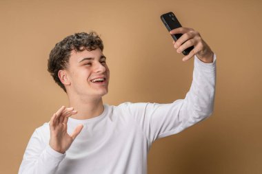Yetişkin bir beyaz erkek stüdyo stüdyosu mutlu bir gülücük attı cep telefonuyla konuşan bir telefon görüşmesi yaptı ya da bej arka plandaki selfie fotokopisini çekti.