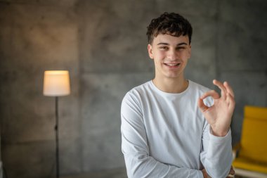 20 yaşındaki beyaz bir adamın portresi. Evinde kameraya bakıp gülümsüyor. Günlük beyaz gömlek giyip fotokopi çekiyor.