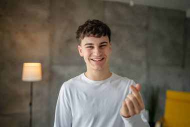 20 yaşındaki beyaz bir adamın portresi. Evinde kameraya bakıp gülümsüyor. Günlük beyaz gömlek giyip fotokopi çekiyor.