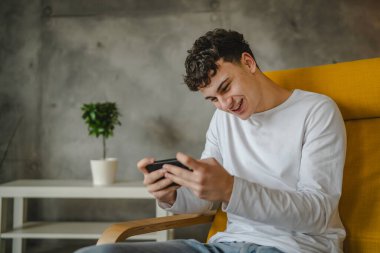 Bir genç çocuk evde video oyunu oynamak için cep telefonu kullanıyor.