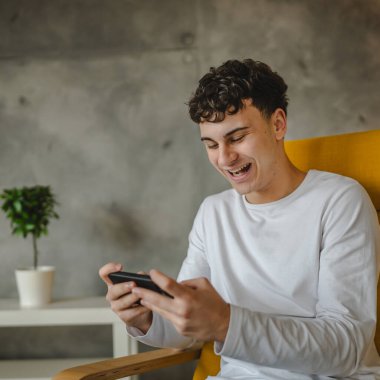 Bir genç çocuk evde video oyunu oynamak için cep telefonu kullanıyor.