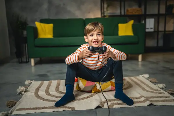 人の少年が自宅に座ってジョイスティック コントローラーの遊びコンソール ビデオゲーム — ストック写真