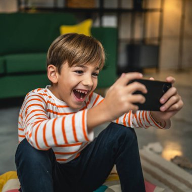 Bir çocuk evde oturuyor cep telefonunu tutuyor akıllı telefon video oyunları oynuyor