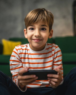 Bir çocuk evde oturuyor cep telefonunu tutuyor akıllı telefon video oyunları oynuyor