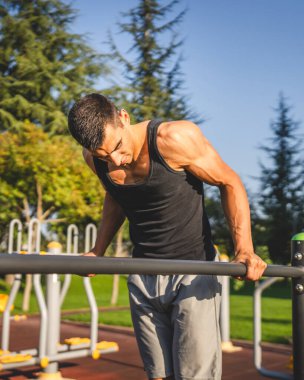 Açık spor salonunda antrenman yapan genç bir beyaz erkek sporcu yaz günü şehirde sağlıklı yaşam tarzı ve dinlenme eğitimi kavramını geliştirir.