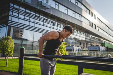 Açık spor salonunda antrenman yapan genç bir beyaz erkek sporcu yaz günü şehirde sağlıklı yaşam tarzı ve dinlenme eğitimi kavramını geliştirir.