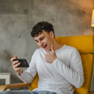 Genç bir çocuğun portresi evde oturup evde online video yayını izlemek için akıllı telefon kullanıyor.