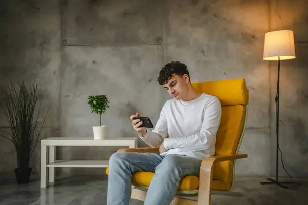 Portrait of teenage boy sit at home use smartphone to watch online video podcast at home