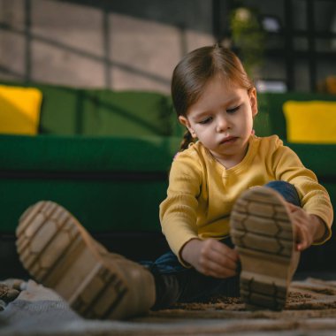 girl toddler child puts on her own boots in the winter at home