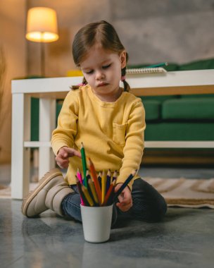 Küçük beyaz kız evde pastel boyalarla oynuyor.