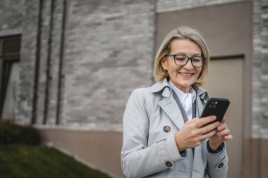 Modern bir kadın şehirde yetişkin bir kadın cep telefonu kullanıyor kısa mesajlar yolluyor ya da internete takılıyor gözlüklü sarışın bir kadın.